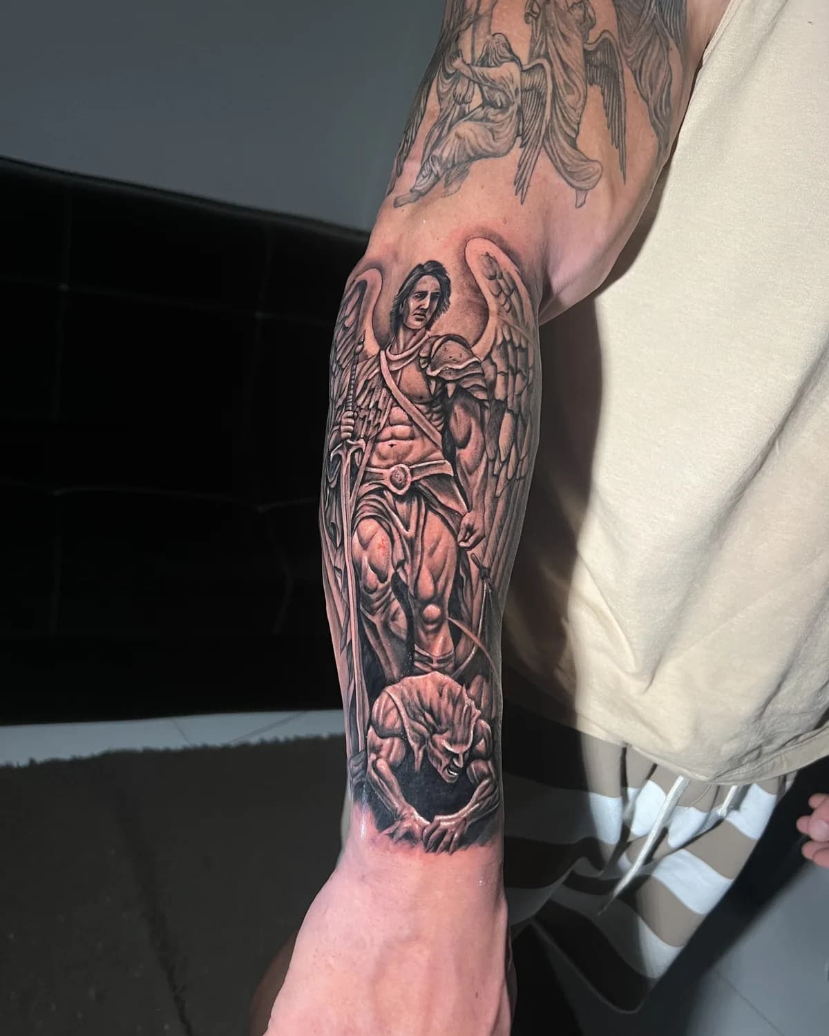 Braço fechado de tatuagem realista com anjos e São Miguel Arcanjo em preto e cinza