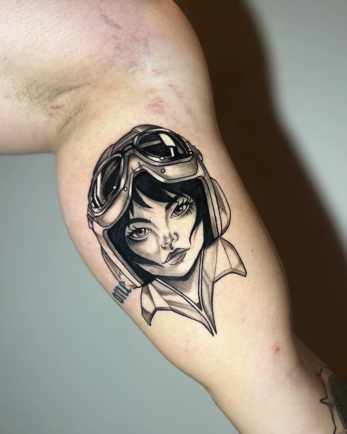 Tatuagem neo-tradicional de menina com capacete de aviadora e avião de papel, no braço