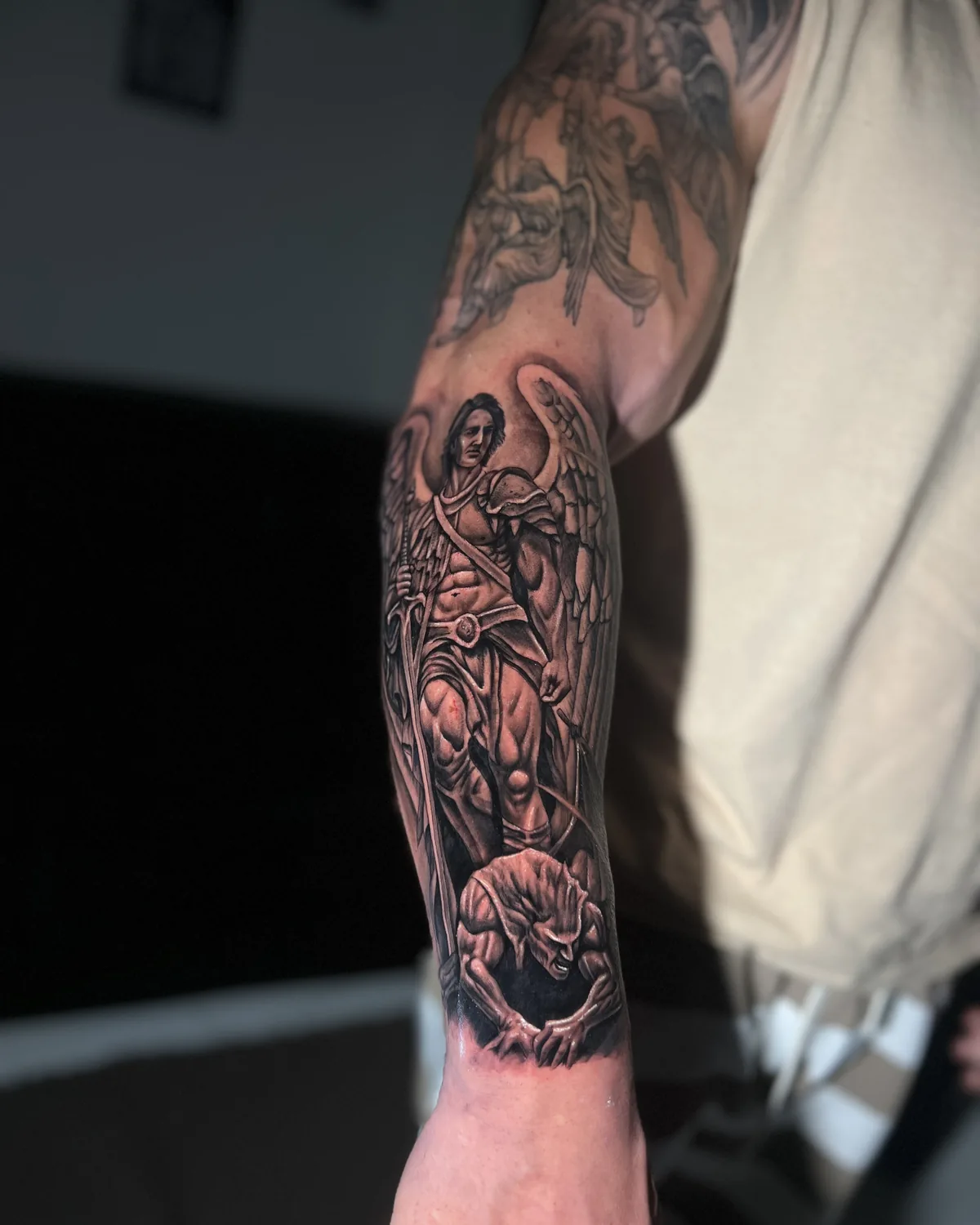 Tatuagem realista de São Miguel Arcanjo com espada, em braço fechado preto e cinza